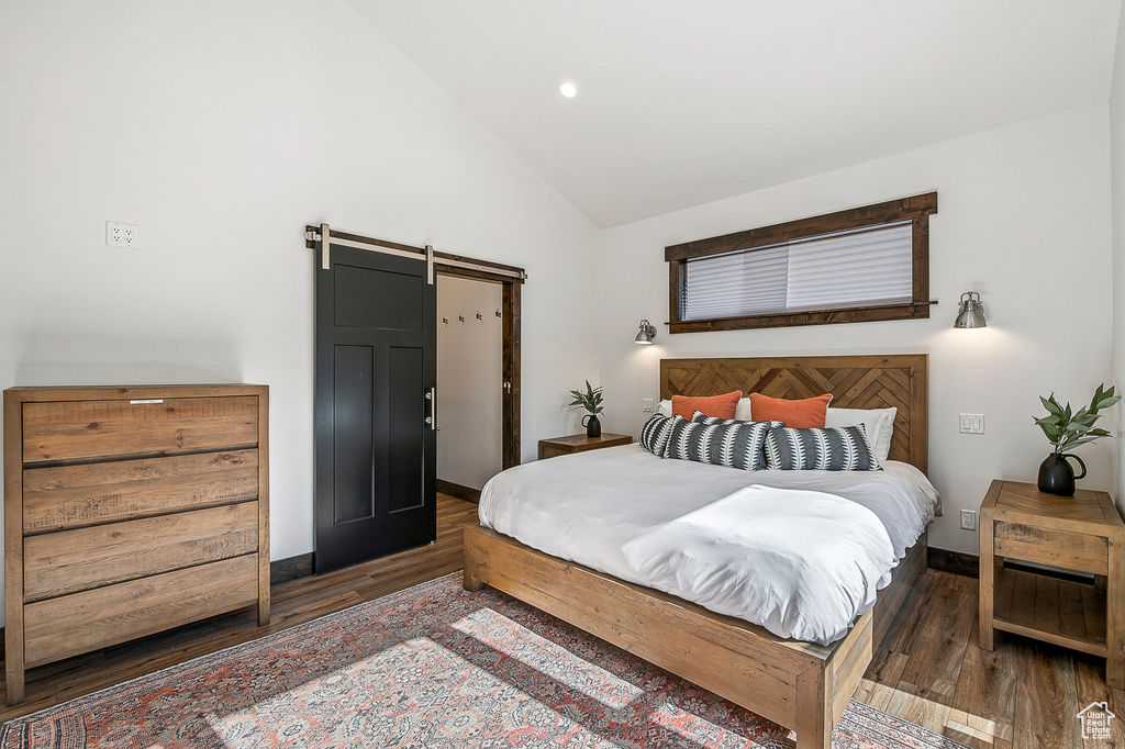 Bedroom with dark hardwood / wood-style flooring, high vaulted ceiling, and a barn door