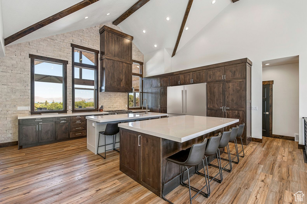 Kitchen with high end refrigerator, high vaulted ceiling, a kitchen island, light hardwood / wood-style flooring, and a kitchen breakfast bar