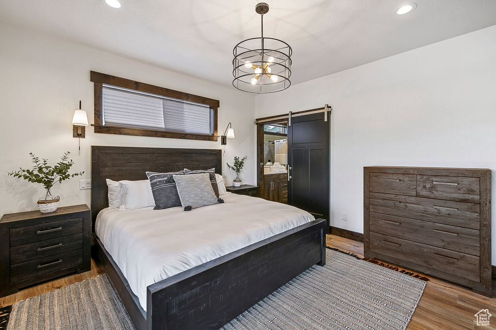 Bedroom with an inviting chandelier, a barn door, dark hardwood / wood-style floors, and ensuite bath