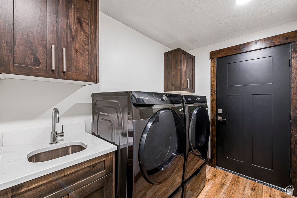 Washroom featuring sink, light hardwood / wood-style flooring, independent washer and dryer, and cabinets