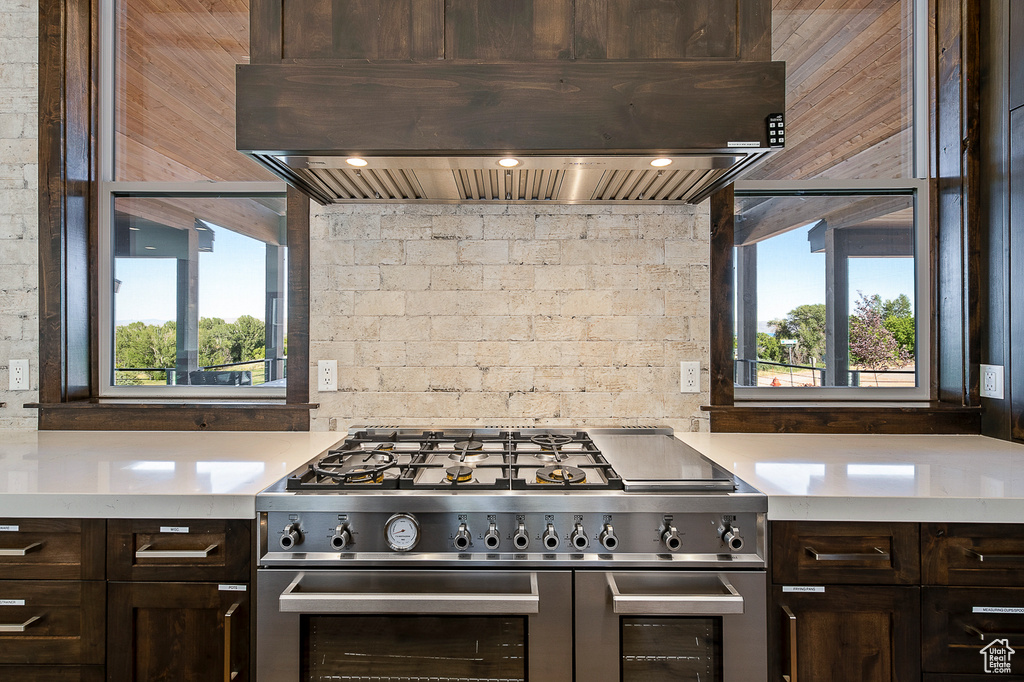 Kitchen with backsplash, custom range hood, dark brown cabinets, and range with two ovens
