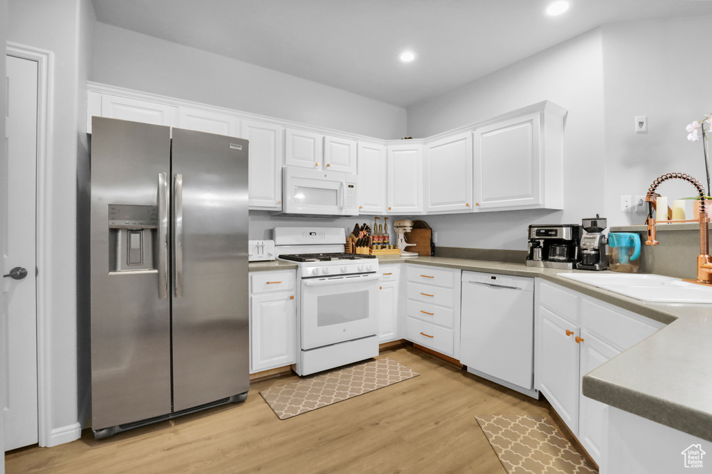 Kitchen with white appliances, light hardwood / wood-style floors, and white cabinets