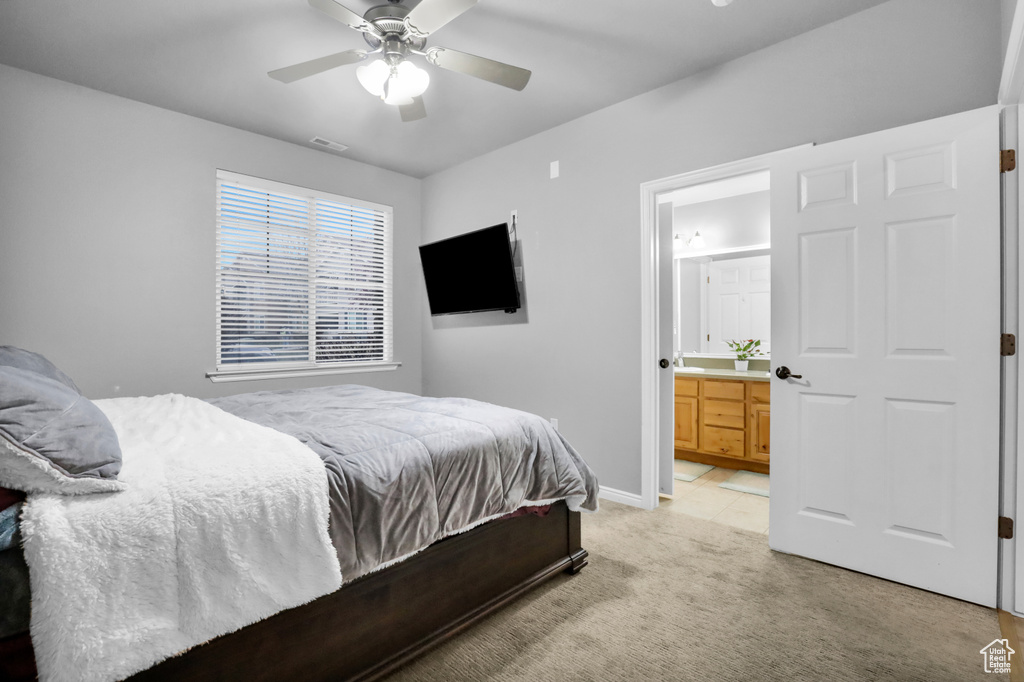Bedroom with ensuite bathroom, ceiling fan, and light colored carpet