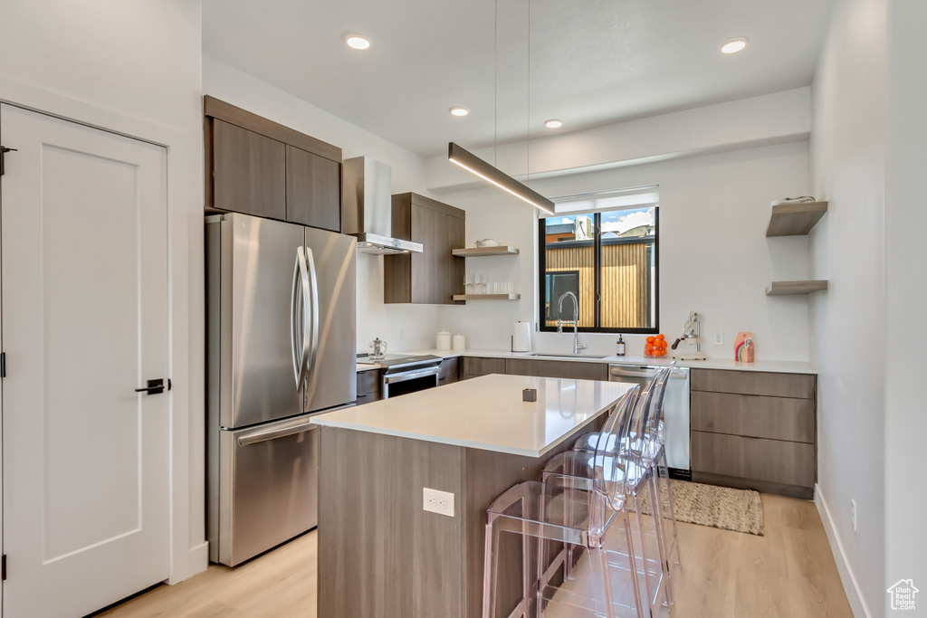 Kitchen featuring wall chimney exhaust hood, appliances with stainless steel finishes, light hardwood / wood-style floors, and a breakfast bar area