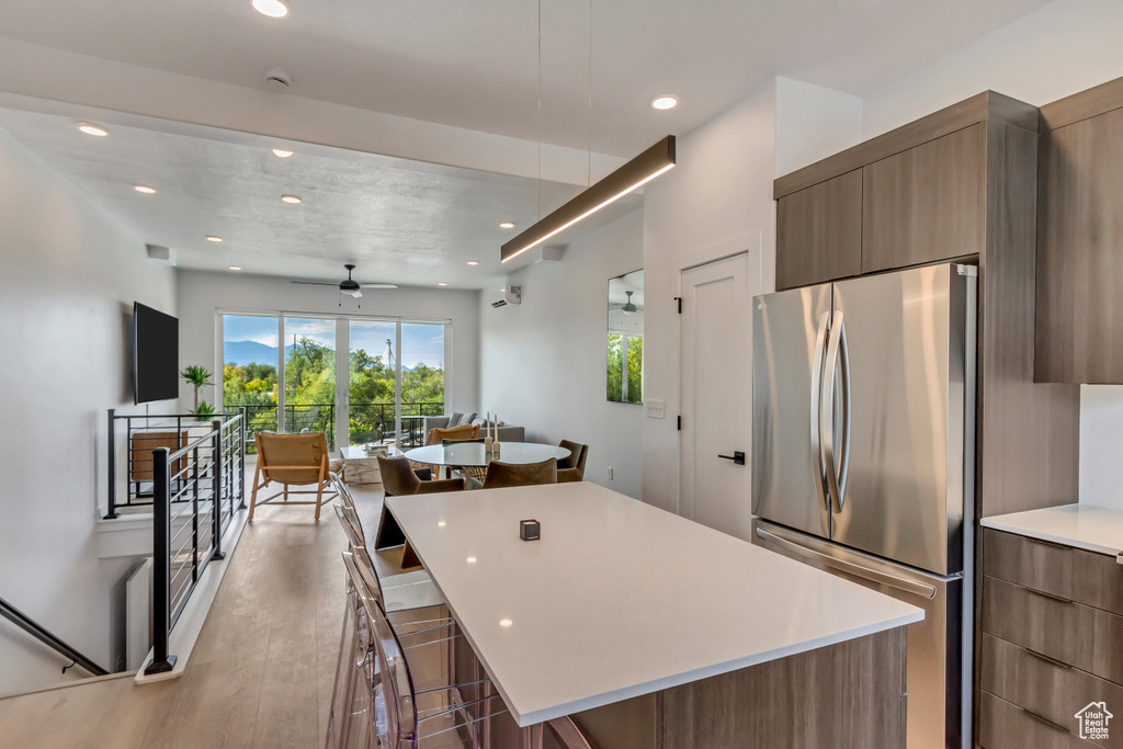 Kitchen featuring light hardwood / wood-style floors, a kitchen island, ceiling fan, stainless steel fridge, and a breakfast bar