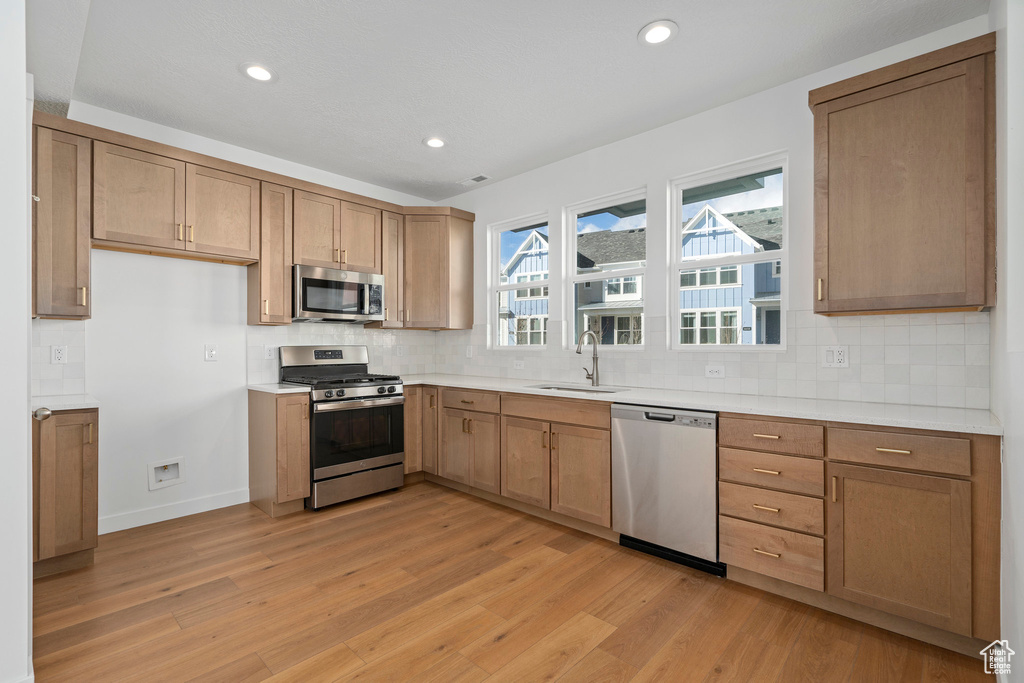 Kitchen with tasteful backsplash, sink, appliances with stainless steel finishes, and light wood-type flooring
