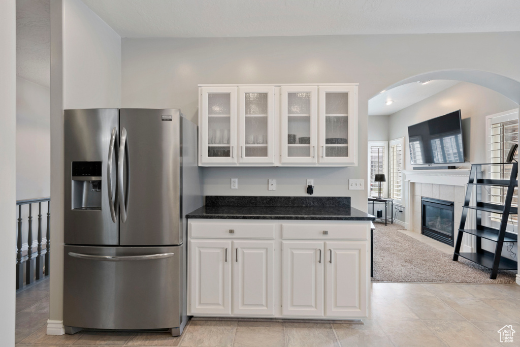 Kitchen with white cabinets, a fireplace, light tile flooring, and stainless steel fridge with ice dispenser