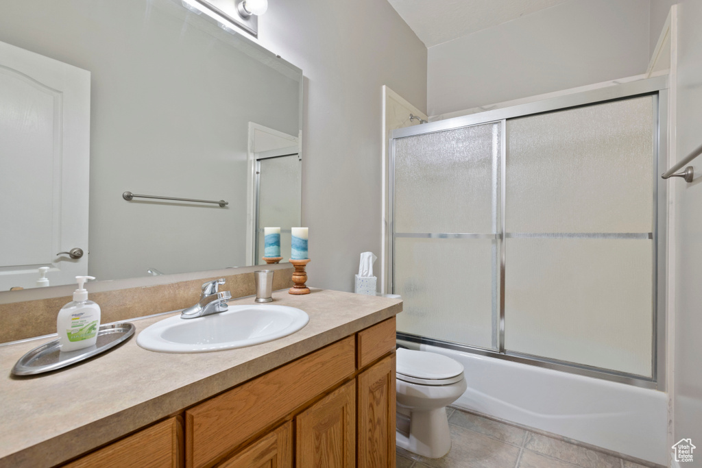 Full bathroom with bath / shower combo with glass door, large vanity, tile floors, and toilet