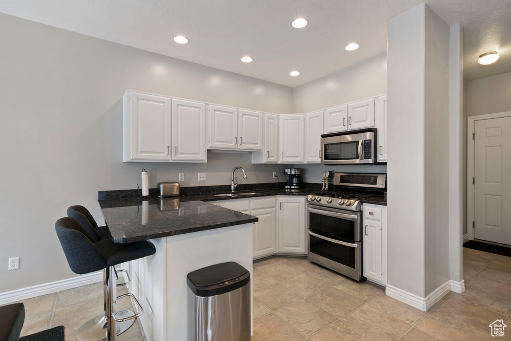 Kitchen featuring white cabinetry, appliances with stainless steel finishes, a kitchen bar, and kitchen peninsula