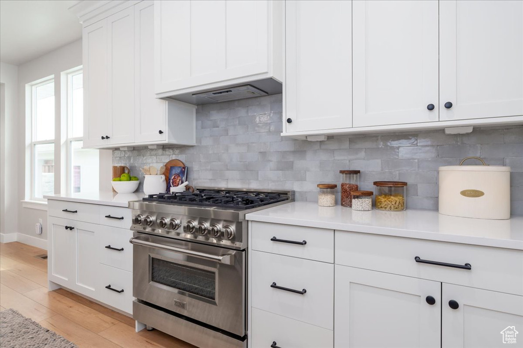 Kitchen featuring white cabinets, high end range, a healthy amount of sunlight, and light wood-type flooring