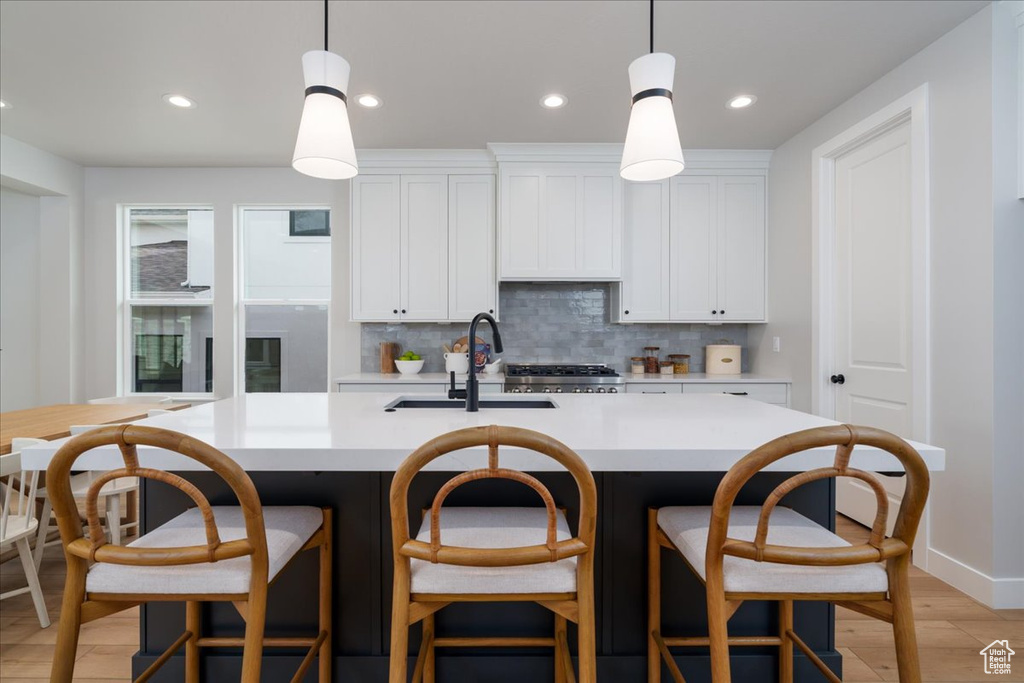 Kitchen with a kitchen island with sink, hanging light fixtures, white cabinetry, and light wood-type flooring