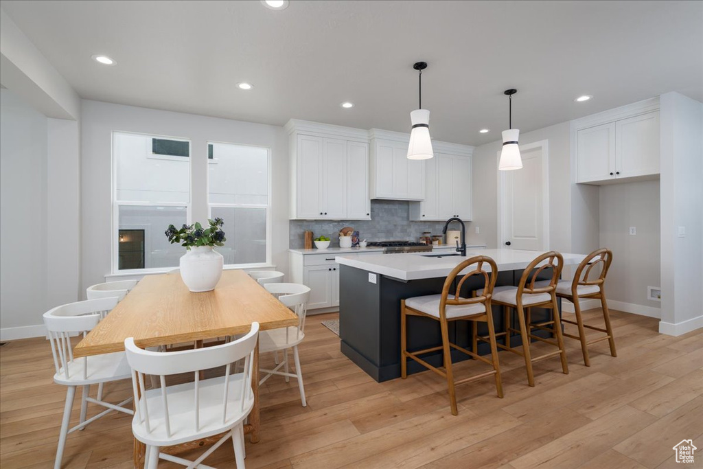 Kitchen with a kitchen bar, light wood-type flooring, white cabinets, a center island with sink, and pendant lighting