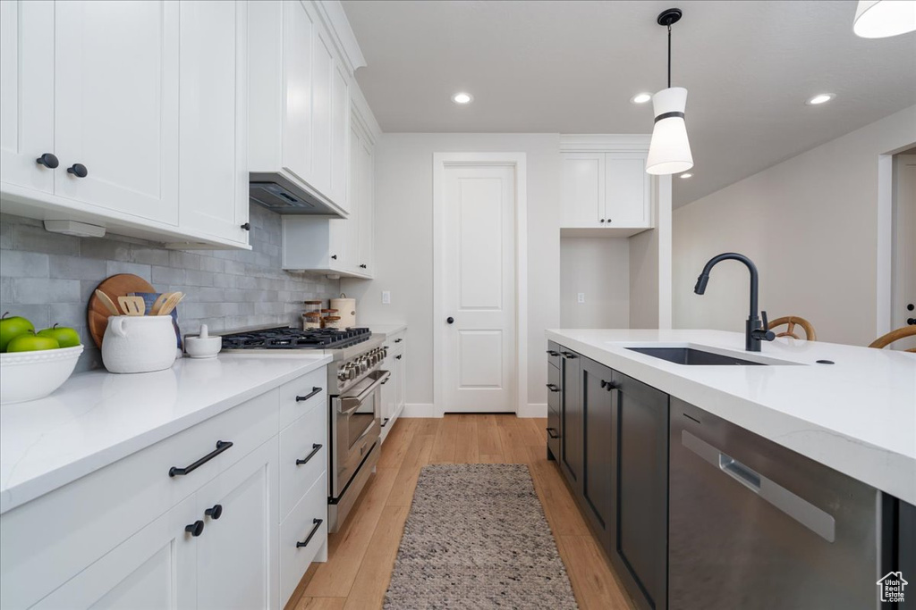 Kitchen with appliances with stainless steel finishes, decorative light fixtures, backsplash, and white cabinetry