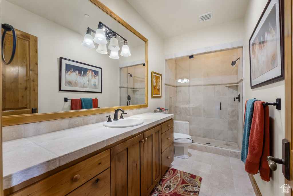 Bathroom with a tile shower, toilet, vanity with extensive cabinet space, and tile floors
