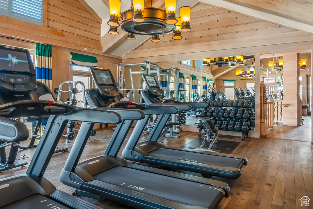 Gym with an inviting chandelier, wood walls, hardwood / wood-style floors, and high vaulted ceiling