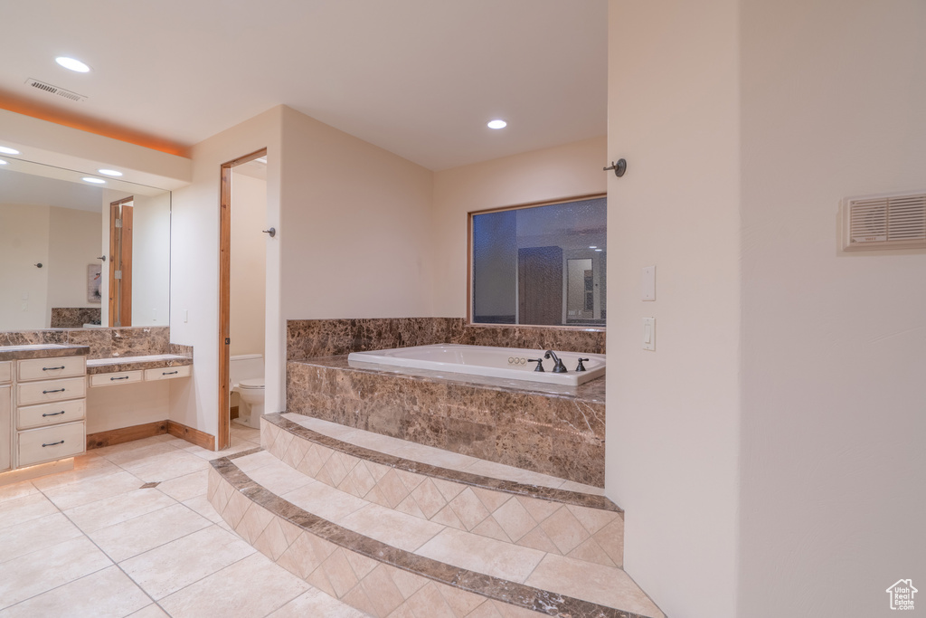 Bathroom with tiled tub, vanity, tile flooring, and toilet