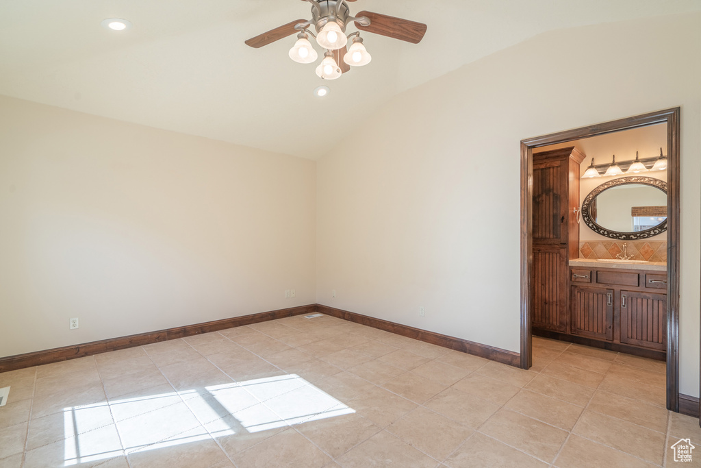 Unfurnished bedroom featuring light tile floors, ensuite bathroom, ceiling fan, and lofted ceiling