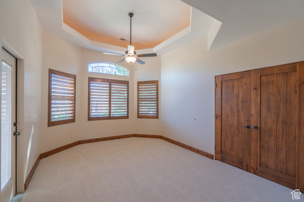 Unfurnished bedroom featuring light carpet, ceiling fan, a tray ceiling, and a closet