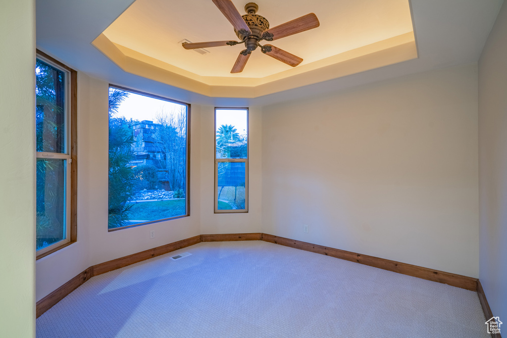 Unfurnished room featuring light colored carpet, ceiling fan, and a raised ceiling