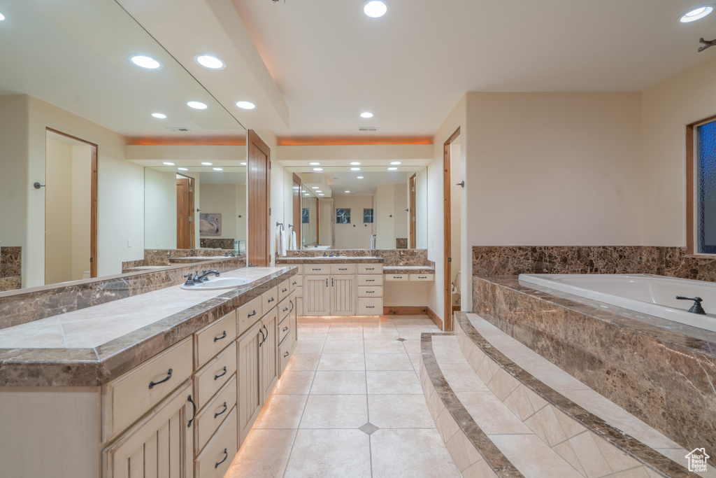 Bathroom featuring large vanity, tiled tub, and tile floors