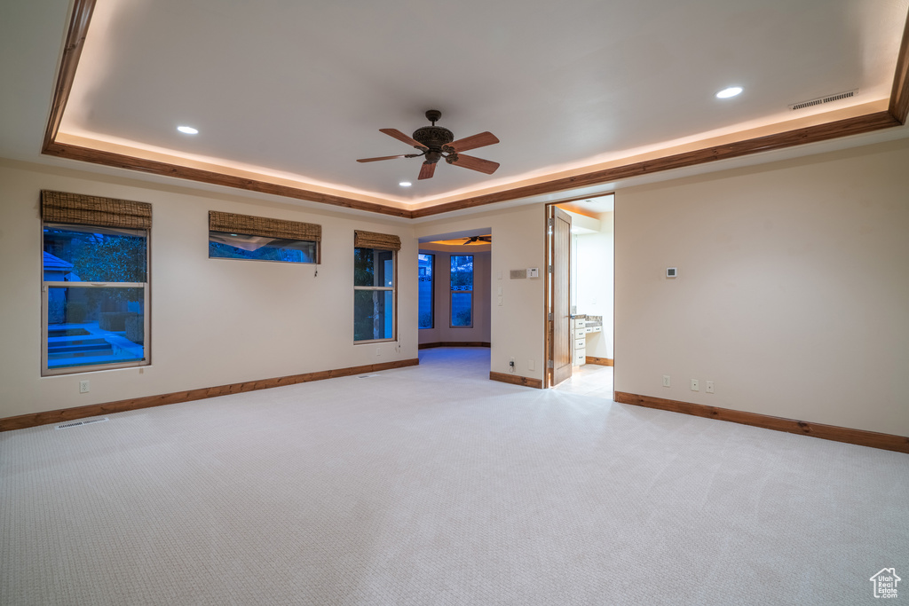 Spare room with light carpet, a raised ceiling, and ceiling fan