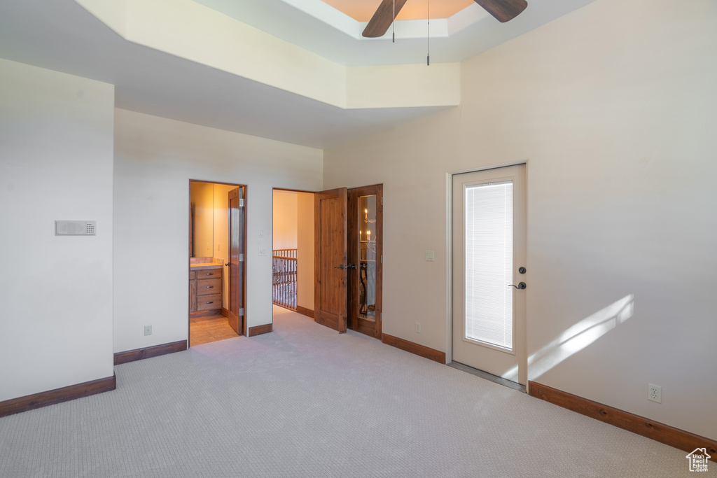 Unfurnished bedroom with a towering ceiling, ceiling fan, light carpet, a tray ceiling, and ensuite bath