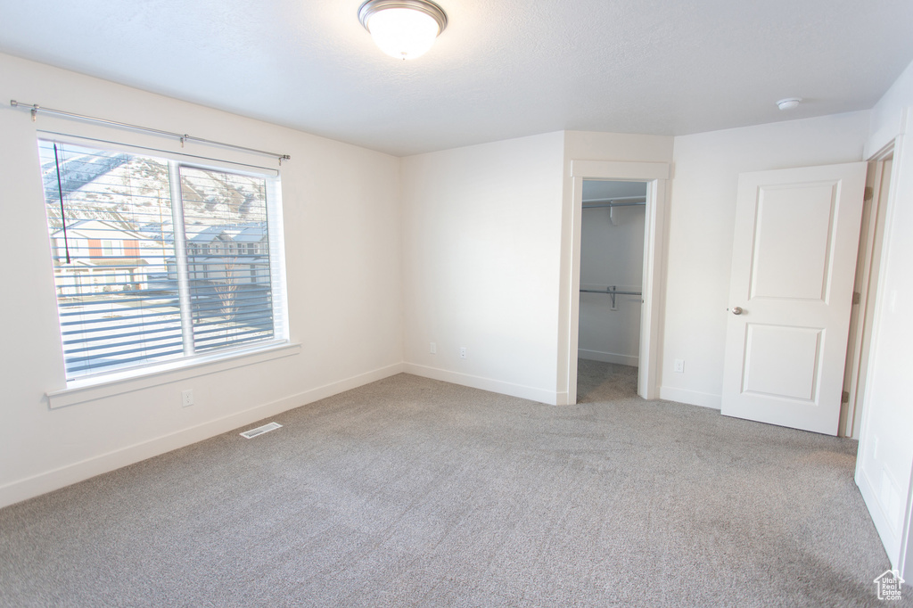 Unfurnished bedroom with a spacious closet, light colored carpet, and a closet