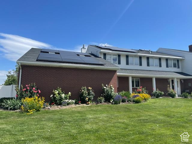 Rear view of property featuring solar panels and a lawn