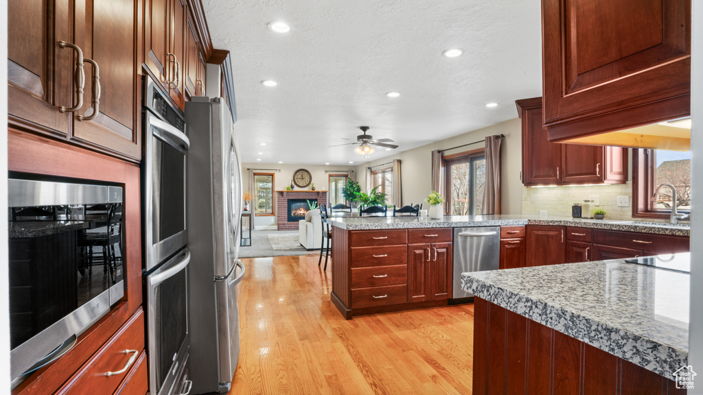 Kitchen with a fireplace, tasteful backsplash, light hardwood / wood-style floors, sink, and ceiling fan