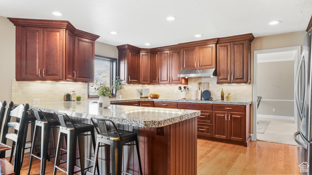 Kitchen with stainless steel fridge, backsplash, a breakfast bar area, kitchen peninsula, and light hardwood / wood-style floors