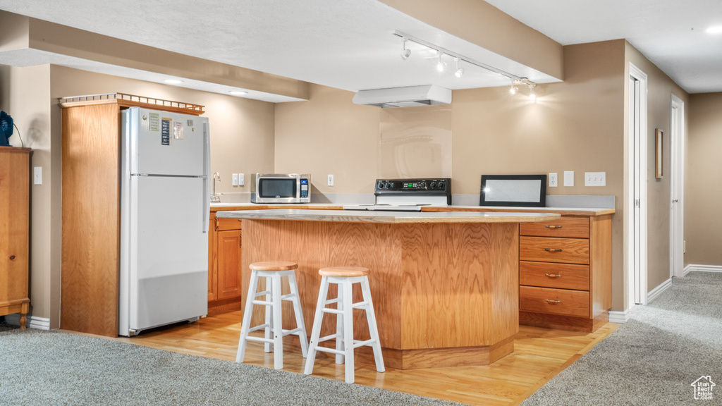Kitchen featuring a center island, track lighting, white fridge, high end black range, and light colored carpet