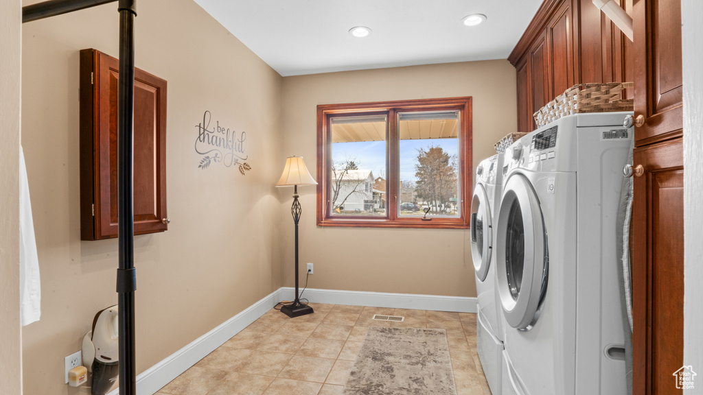 Clothes washing area with washing machine and clothes dryer, light tile floors, and cabinets