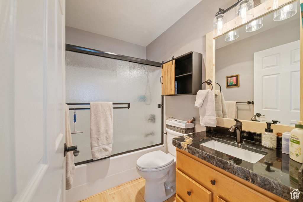 Full bathroom with large vanity, wood-type flooring, toilet, and bath / shower combo with glass door