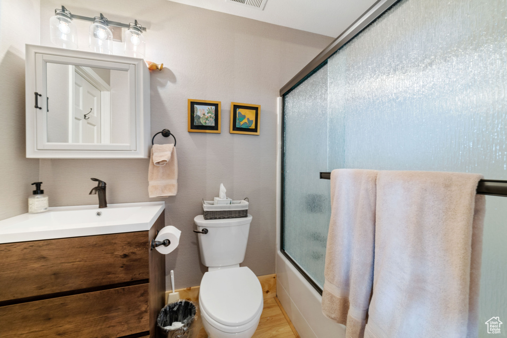 Full bathroom with vanity, toilet, shower / bath combination with glass door, and wood-type flooring