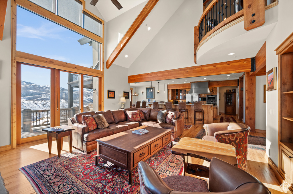 Living room with light hardwood / wood-style floors, ceiling fan, a mountain view, high vaulted ceiling, and beam ceiling