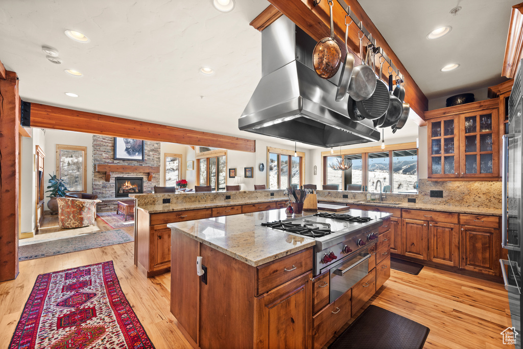 Kitchen featuring a stone fireplace, light stone countertops, backsplash, light hardwood / wood-style floors, and island exhaust hood