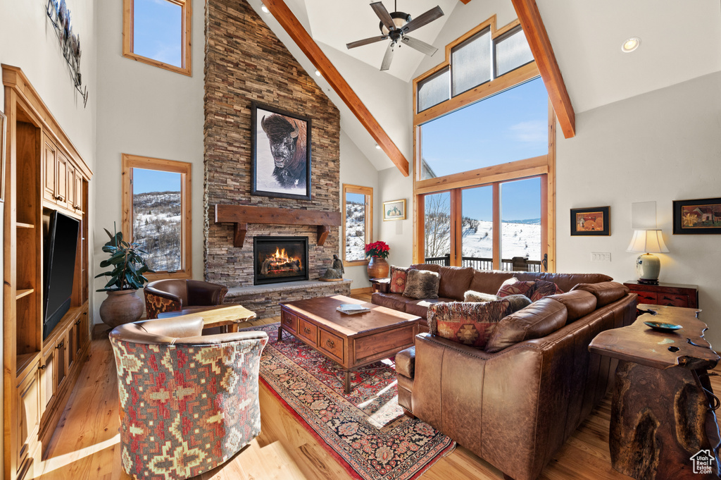 Living room featuring ceiling fan, light hardwood / wood-style flooring, high vaulted ceiling, and a stone fireplace