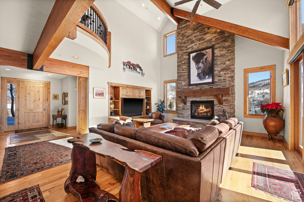 Living room with high vaulted ceiling, a stone fireplace, light hardwood / wood-style floors, beam ceiling, and ceiling fan