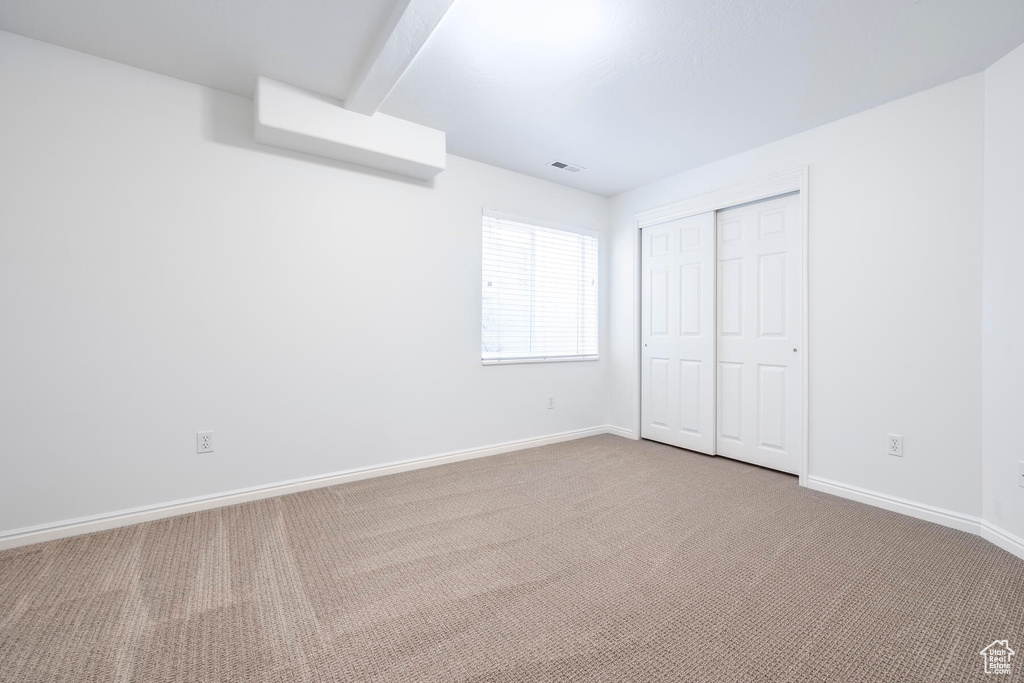 Unfurnished bedroom featuring dark colored carpet, beam ceiling, and a closet