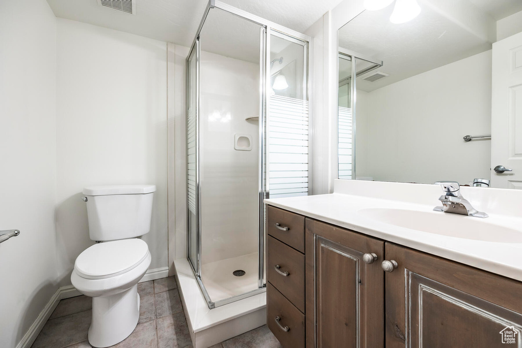 Bathroom featuring vanity, toilet, an enclosed shower, and tile flooring
