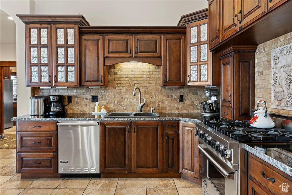 Kitchen with tasteful backsplash, dark stone counters, sink, light tile floors, and stainless steel appliances