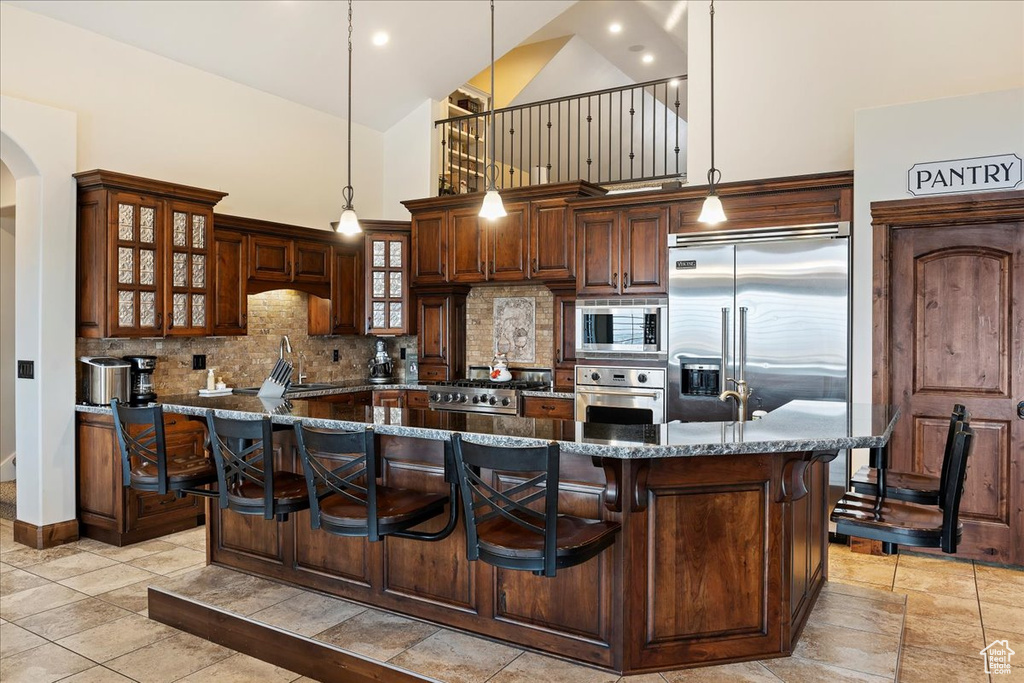 Kitchen with tasteful backsplash, dark stone counters, pendant lighting, high vaulted ceiling, and built in appliances