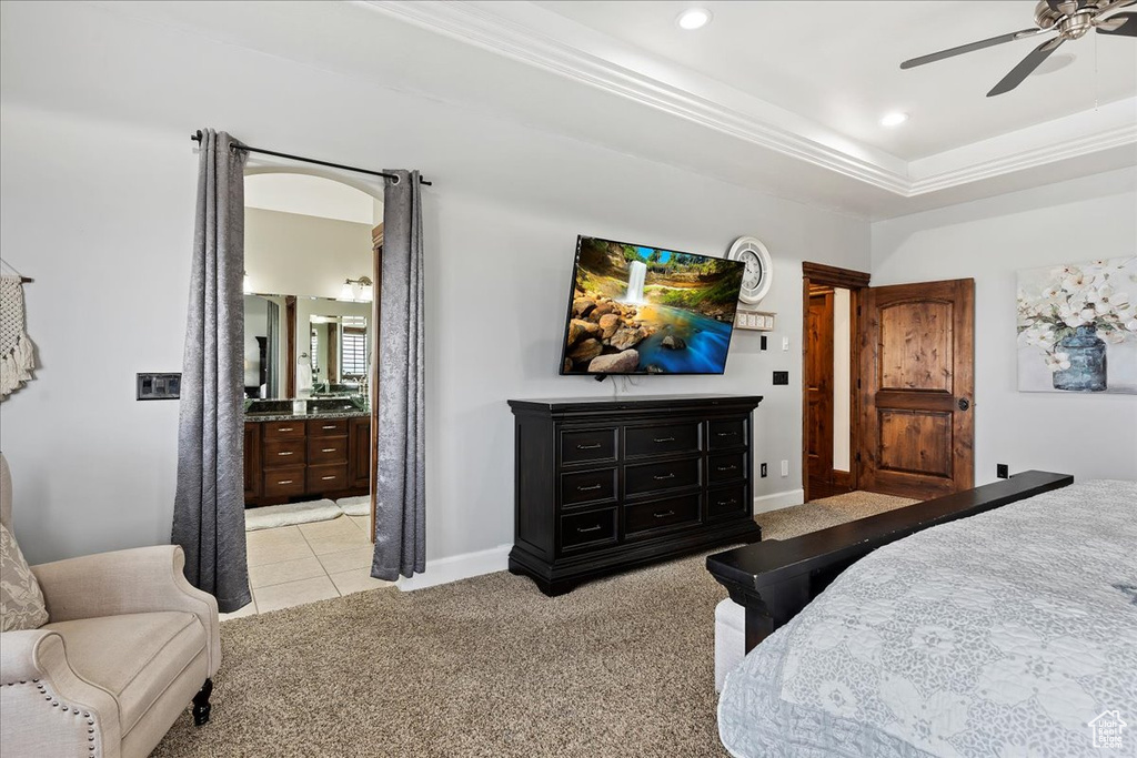 Carpeted bedroom featuring a tray ceiling, ceiling fan, and ensuite bath