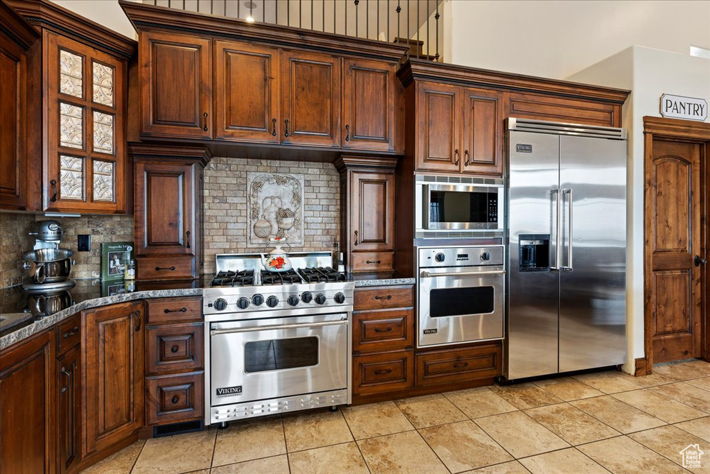Kitchen with built in appliances, light tile floors, dark stone countertops, and tasteful backsplash