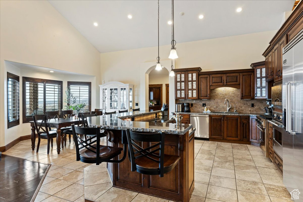 Kitchen with backsplash, hanging light fixtures, light tile floors, dark stone countertops, and stainless steel dishwasher