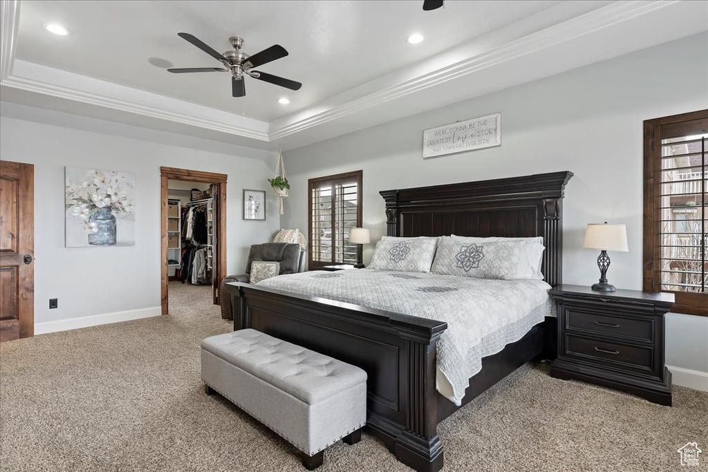 Bedroom featuring a walk in closet, ceiling fan, light colored carpet, and a tray ceiling
