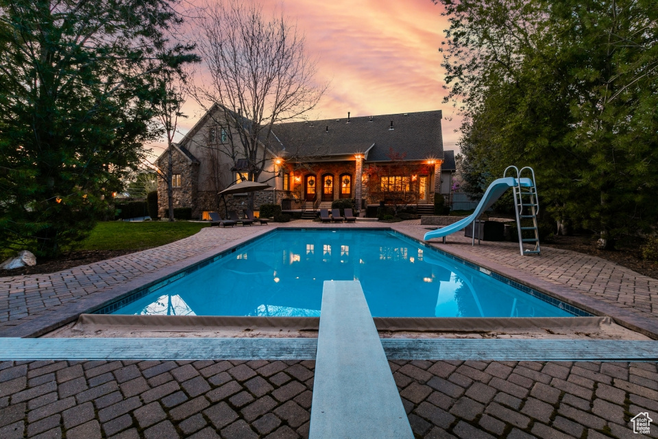 Pool at dusk featuring a water slide, a patio, and a diving board