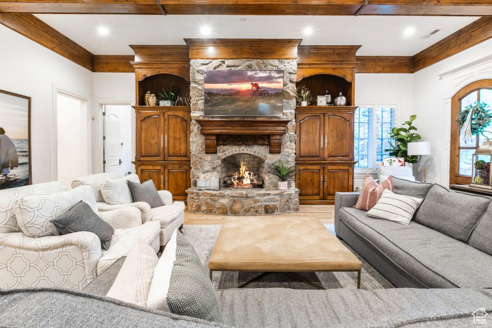 Living room with a stone fireplace, light hardwood / wood-style floors, and crown molding