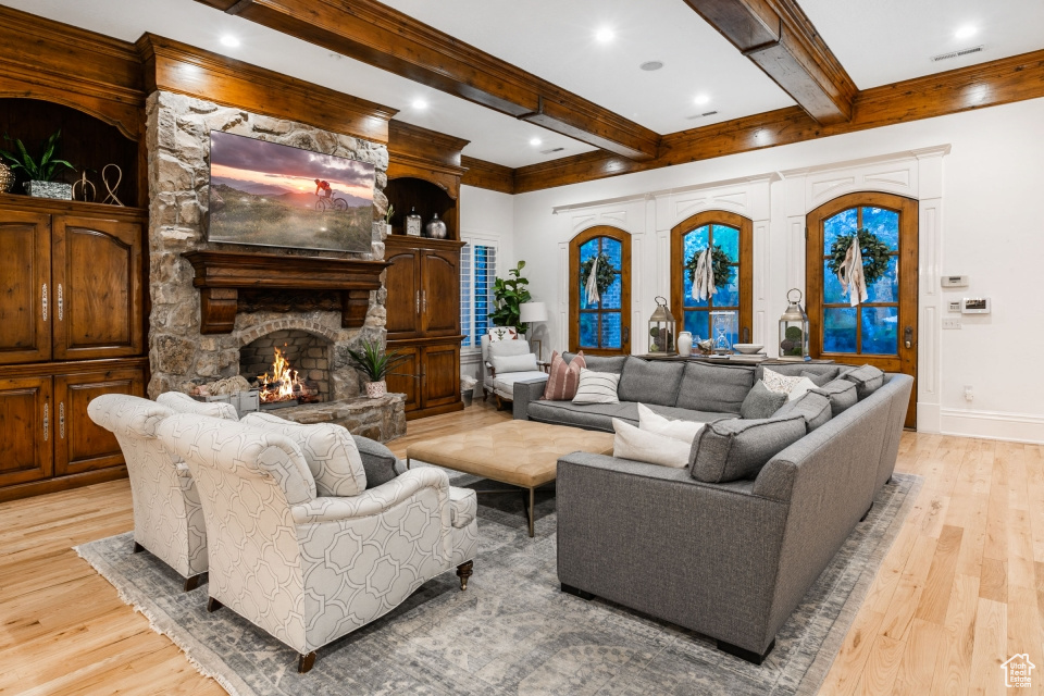 Living room featuring light hardwood / wood-style flooring, beamed ceiling, a stone fireplace, and french doors