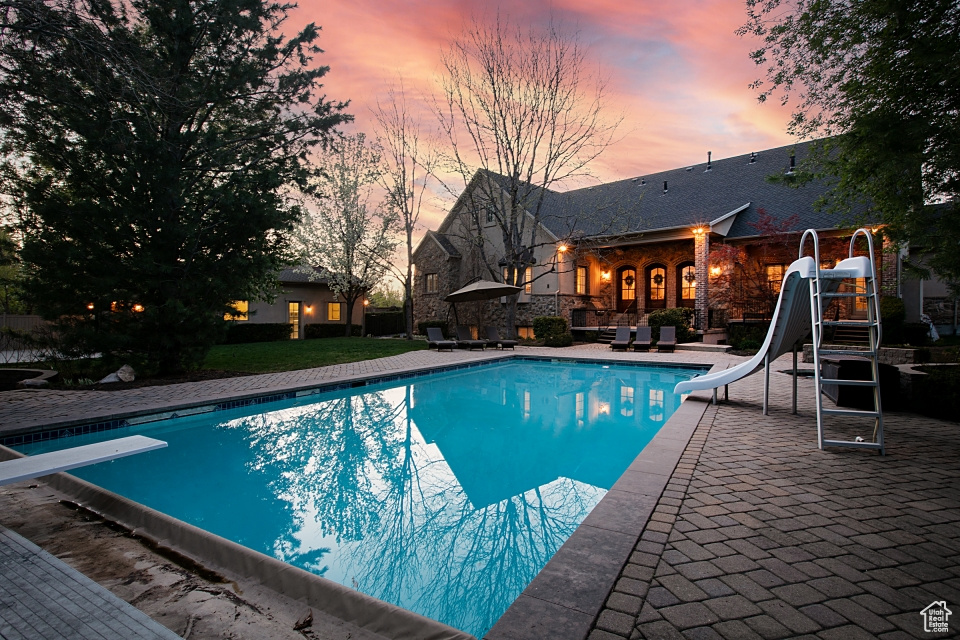 Pool at dusk with a water slide, a patio area, and a diving board